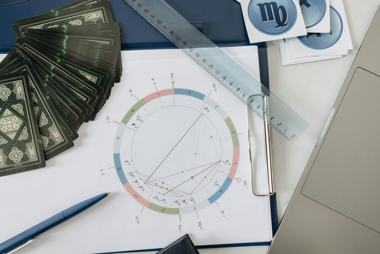 Astrological chart with tarot cards, pen, ruler, and laptop on a table