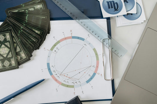 Astrological chart with tarot cards, pen, ruler, and laptop on a table